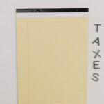 Close-up of a yellow legal pad and the word 'TAXES' on a white surface, ideal for finance themes.