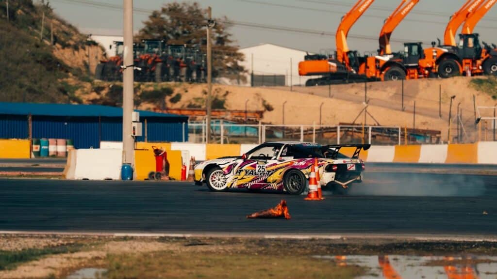 Exciting scene of a colorful drift car maneuvering on a track with construction vehicles in the background.