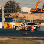 Exciting scene of a colorful drift car maneuvering on a track with construction vehicles in the background.