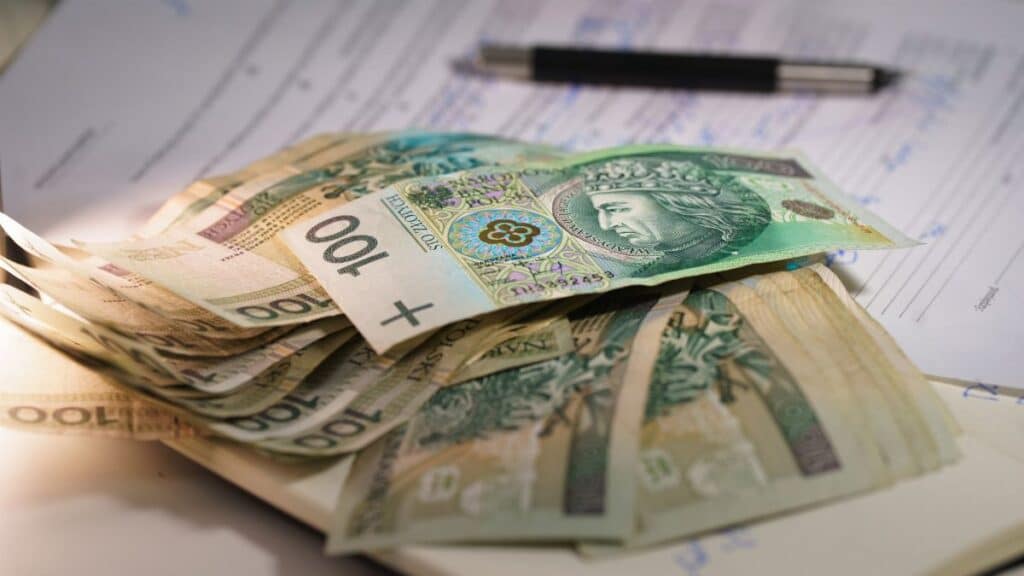 Stack of Polish zloty banknotes on financial documents with a pen, indicating monetary transactions in an office setting.
