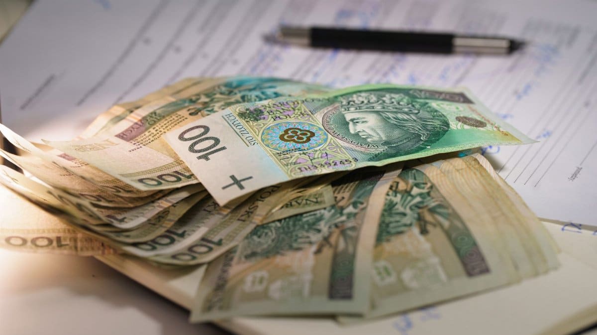 Stack of Polish zloty banknotes on financial documents with a pen, indicating monetary transactions in an office setting.