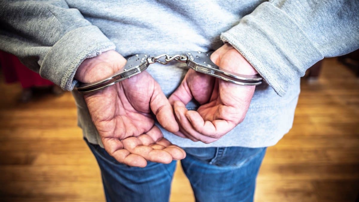 Close-up of a person in handcuffs viewed from behind, wearing casual clothing indoors.
