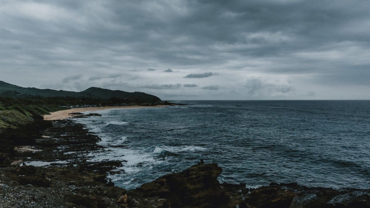 A dramatic view of Hawaiian coastline with storm clouds and rugged rocks.