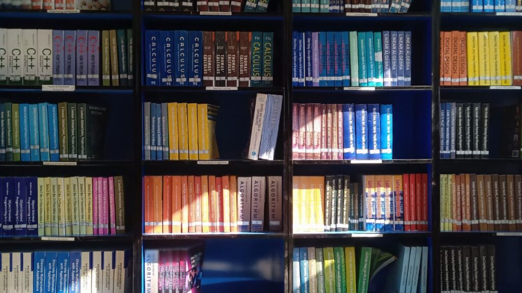 A vibrant library bookshelf displaying a range of educational books organized by subject.