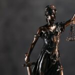 Detailed bronze Lady Justice statue with scales and sword against a dark background, symbolizing law and justice.