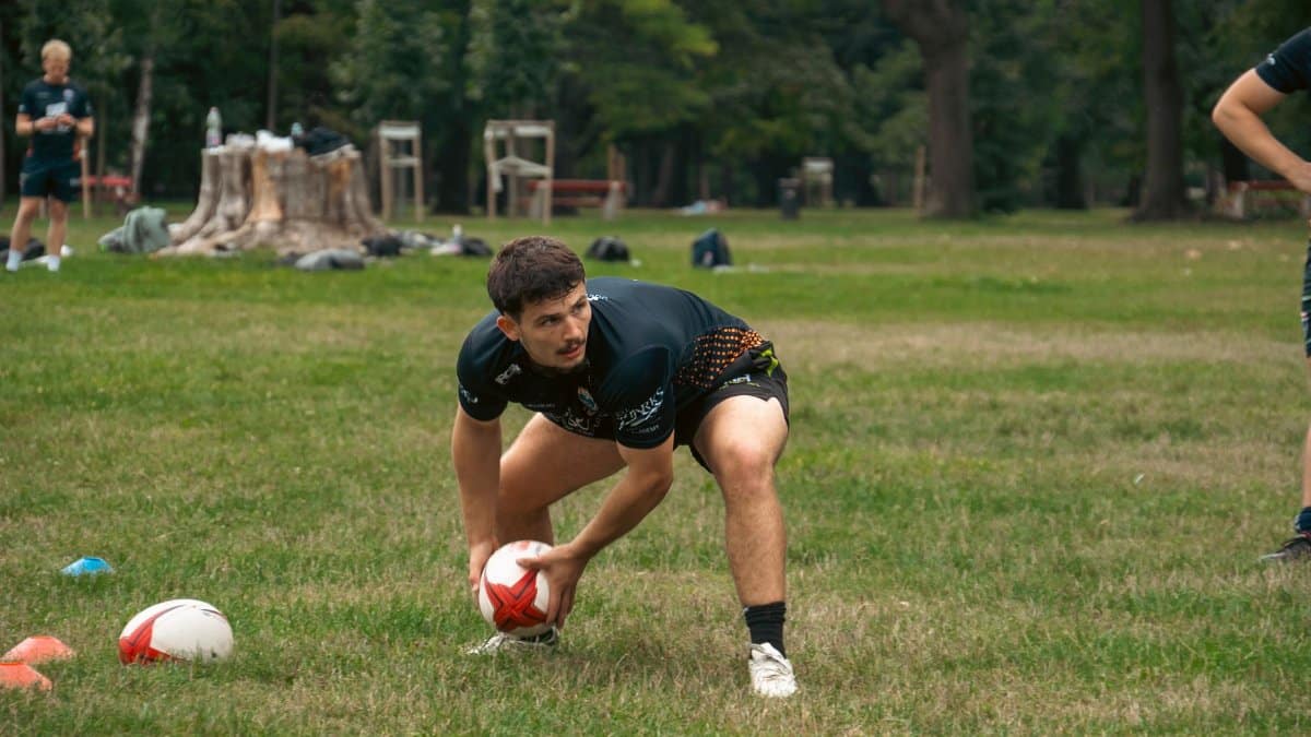 A rugby player practicing in a lush green outdoor park area during the day.