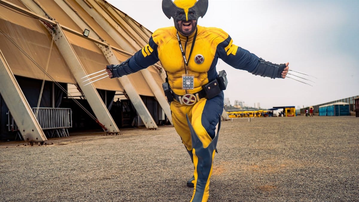 A cosplayer vividly dressed as Wolverine with claws extended outdoors showing excitement.