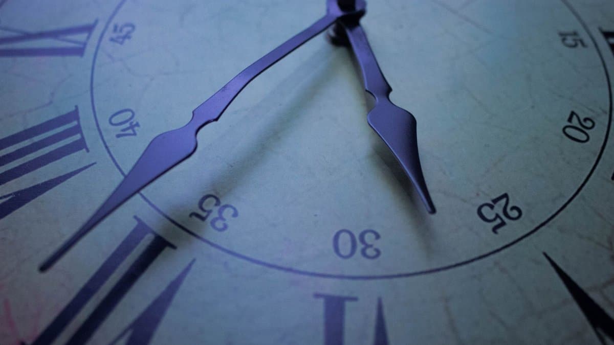 Detailed close-up of a vintage clock face with Roman numerals, focusing on the decorative hands at 30 past.