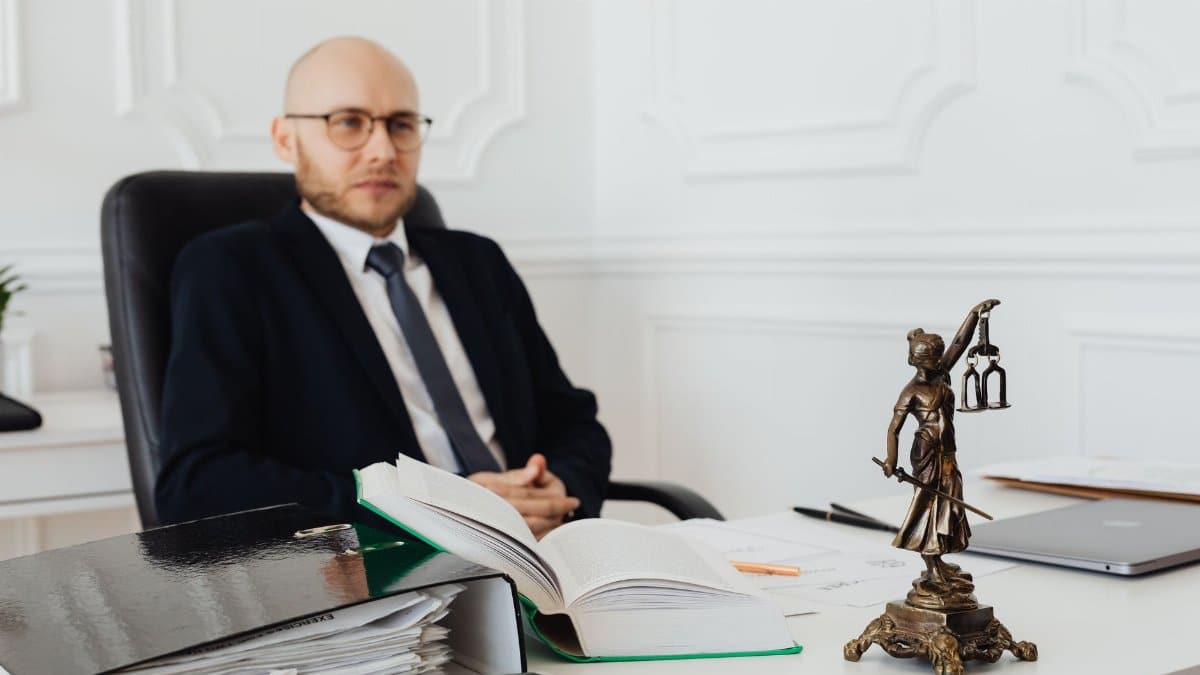 Bald lawyer in office sitting with legal documents and Justice statue.