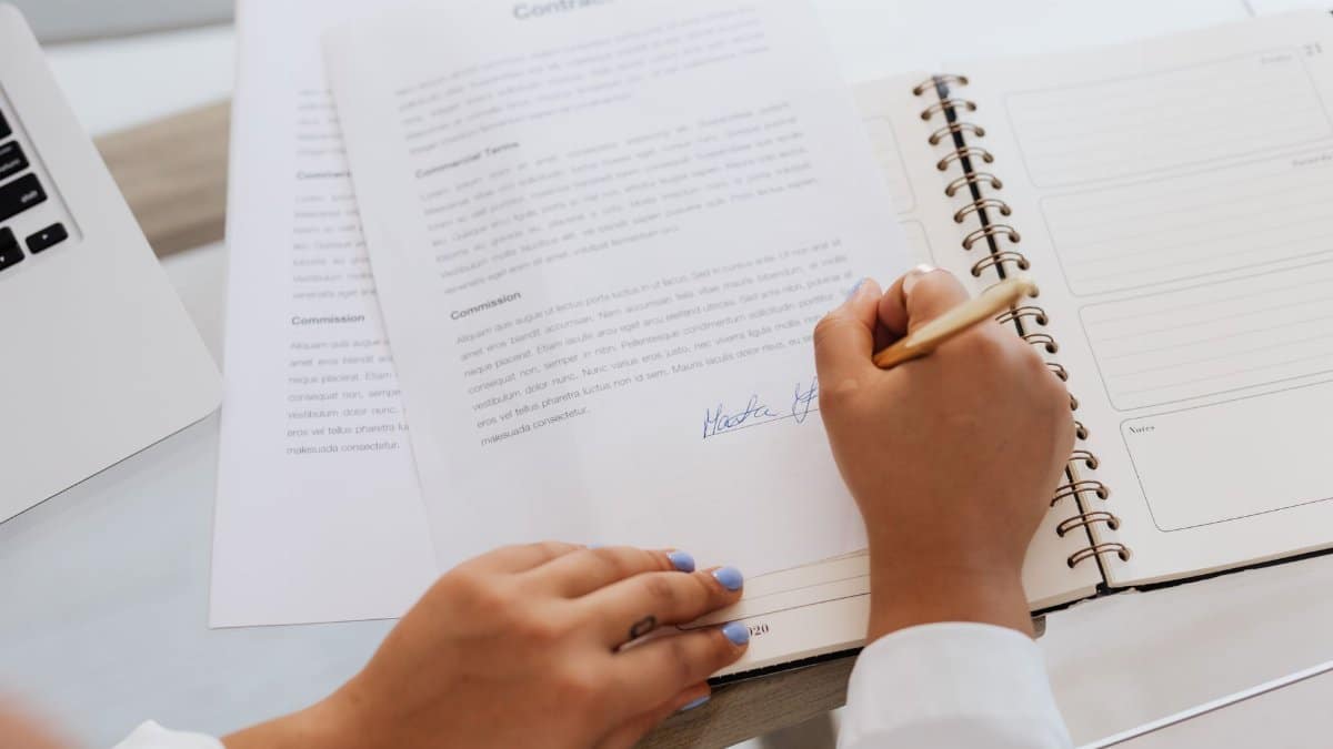 Close-up of hands signing a contract on a desk with office supplies, symbolizing legal agreements.