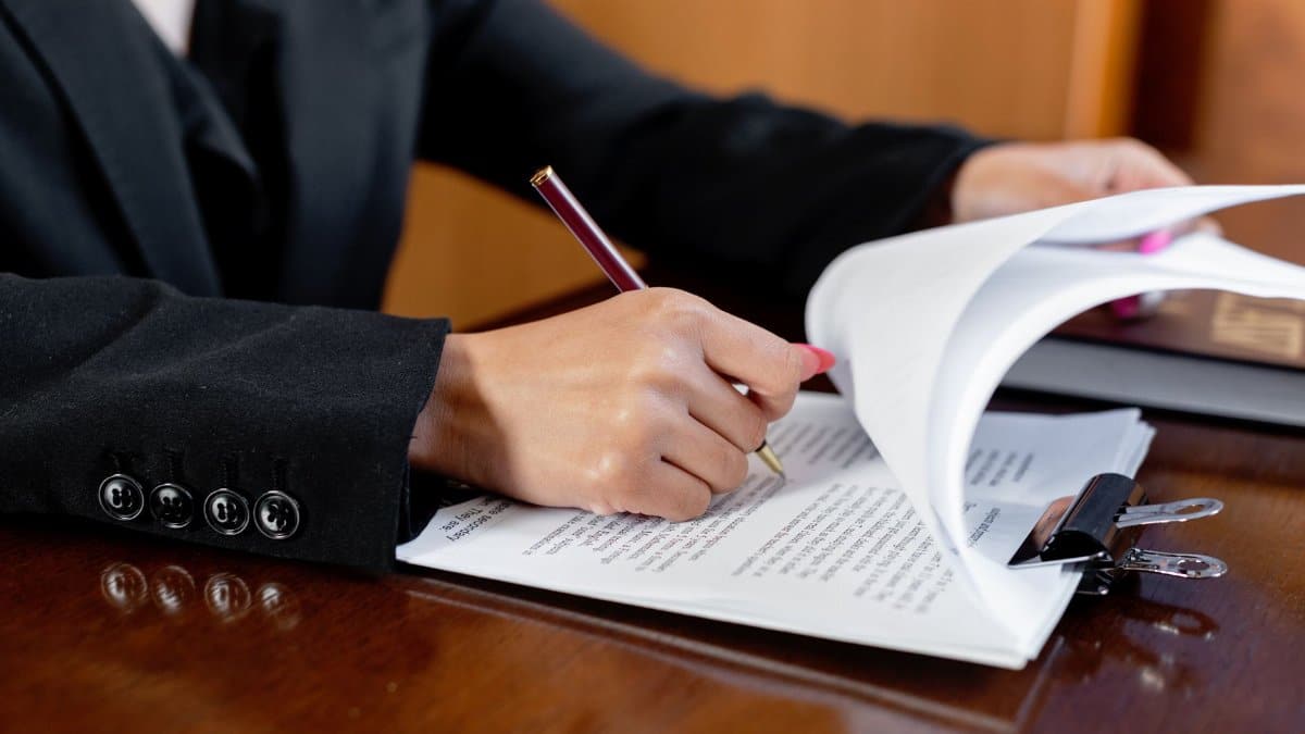 Close-up of a woman signing legal documents with a pen in an office setting.