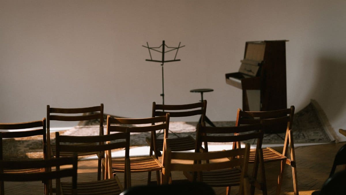 An empty music room with wooden chairs, a piano, and a sheet music stand ready for a performance.