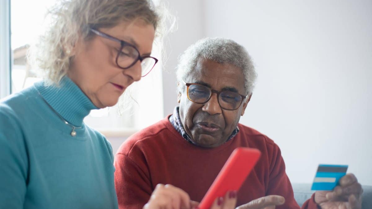 Elderly couple using smartphone and credit card for online shopping indoors.