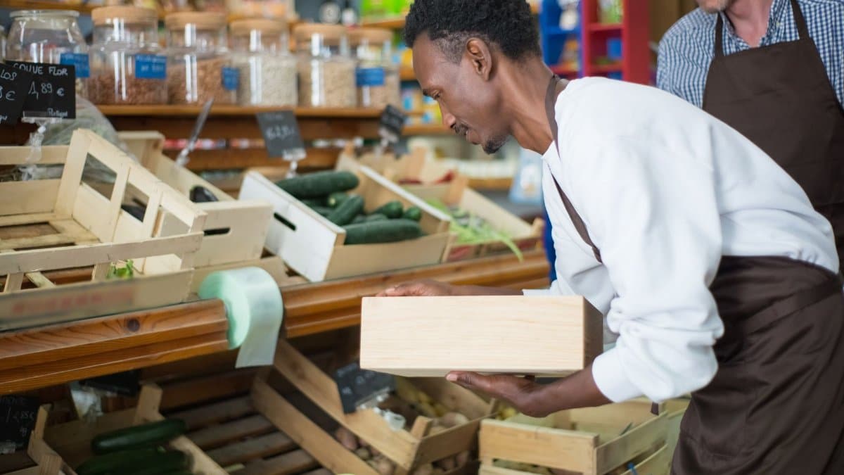 A grocery store worker arranging fresh produce in wooden crates, emphasizing fresh and healthy food.