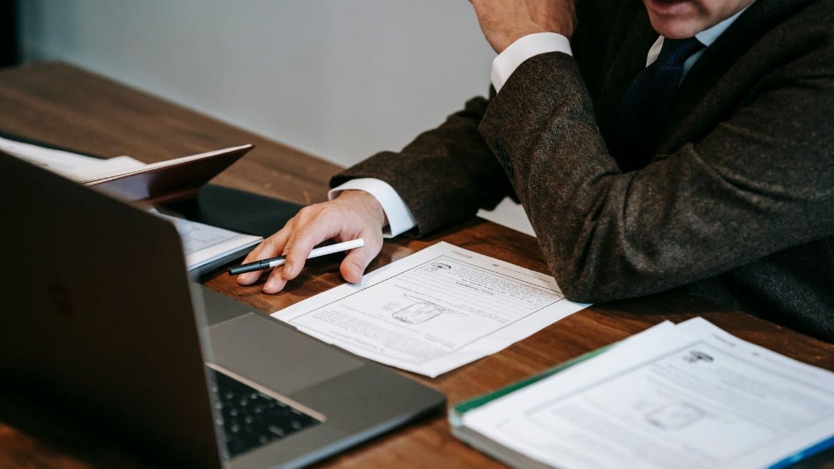 A business professional in formal attire analyzing documents and using a laptop for work indoors.