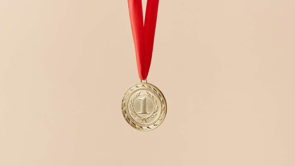 Close-up of a gold medal with a red ribbon on a beige background, symbolizing achievement.