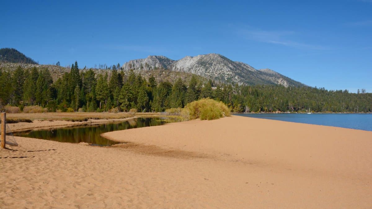 Picturesque view of South Lake Tahoe with sandy beach, evergreen trees, and Sierra Nevada mountains.