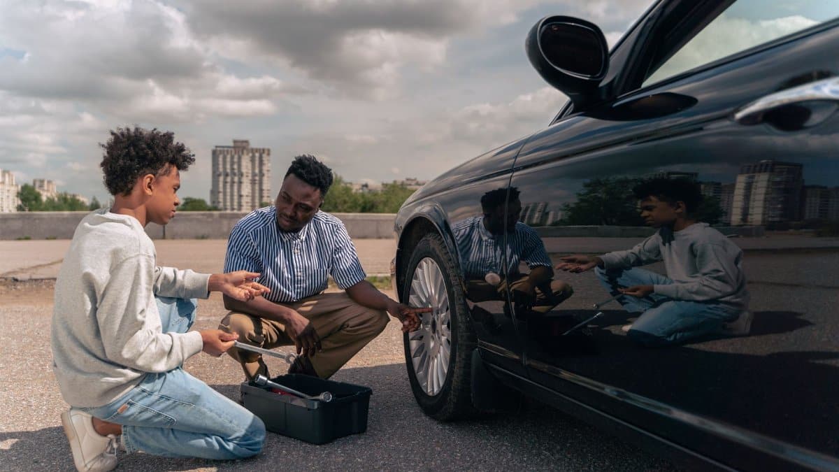 Father and son bonding while learning tire maintenance outdoors. Daytime photo.