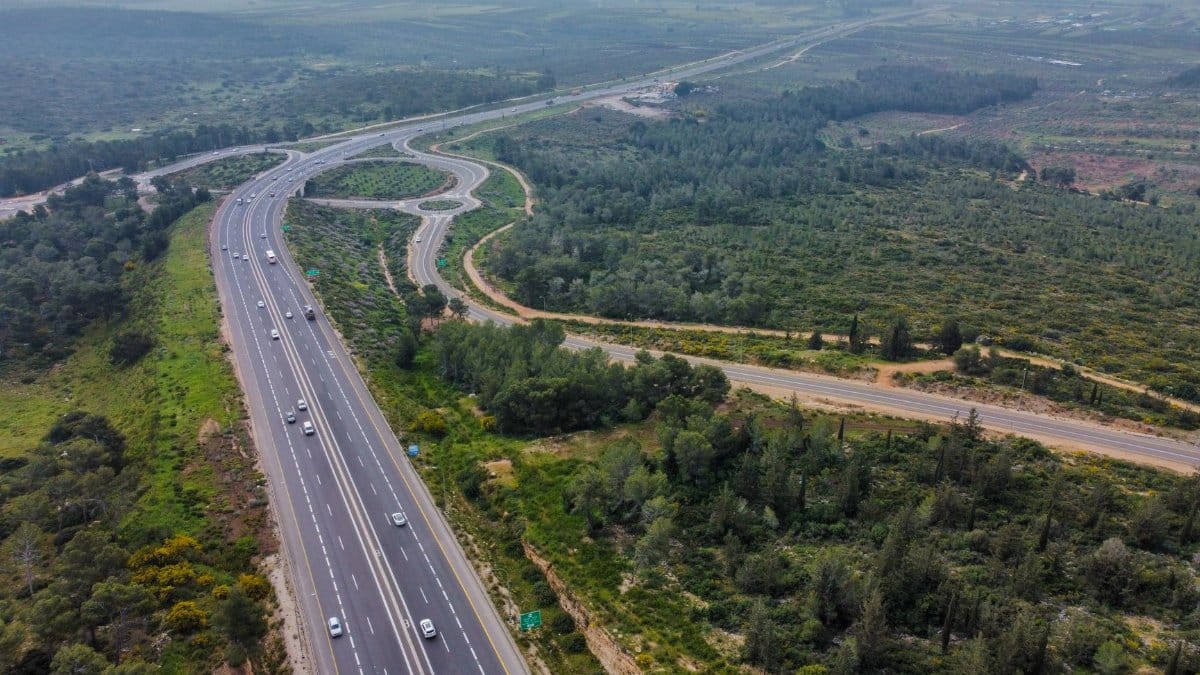 An aerial view of a highway curving through a lush forest landscape.