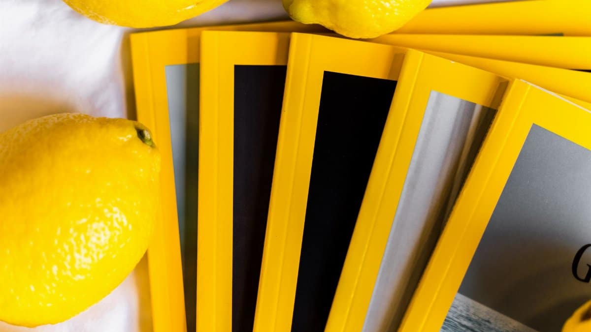 Top view of stack of similar books with yellow edges placed on white table near fresh whole lemons in daylight
