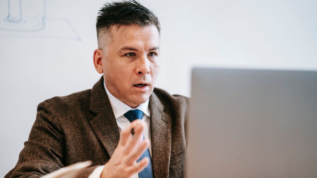 Professional businessman in formal attire engaged in an online meeting using a laptop.