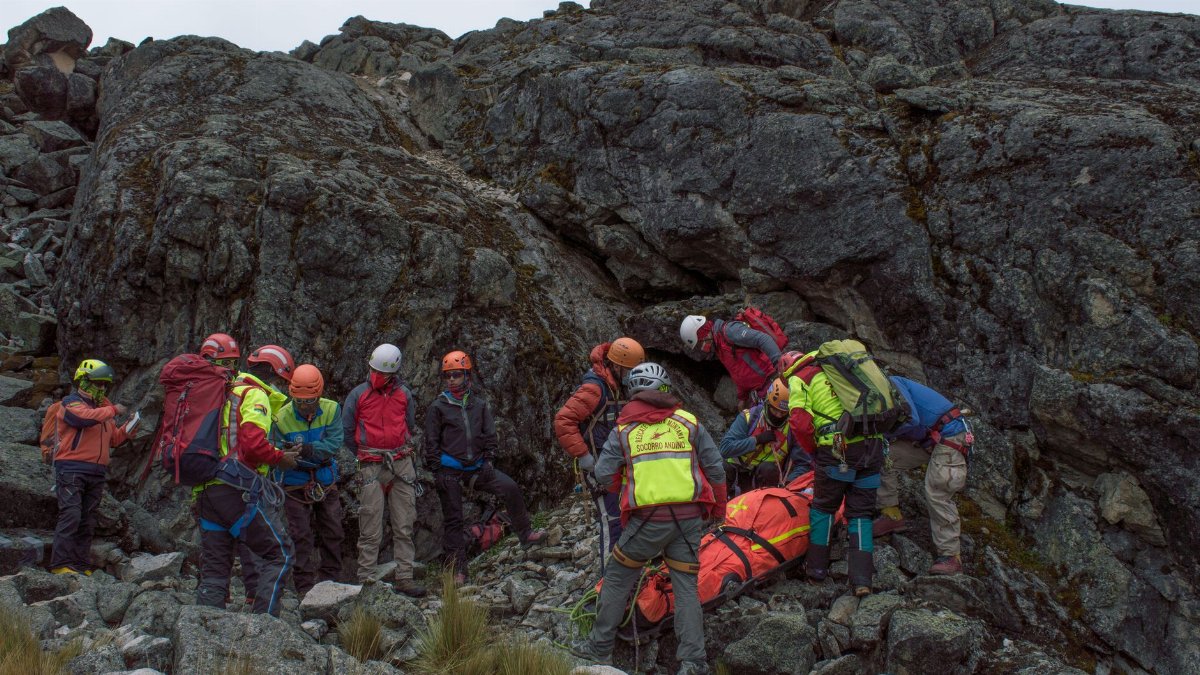 A rescue team aids an injured hiker on a rocky mountain slope during daylight.