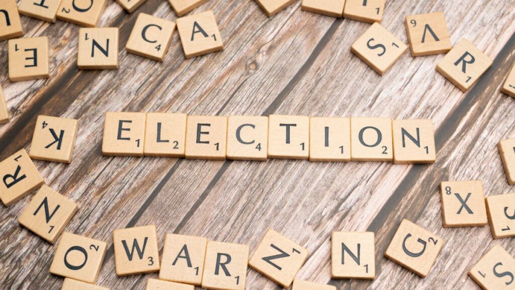 Wooden letter tiles form the word 'election' on a textured wooden surface, symbolizing voting.