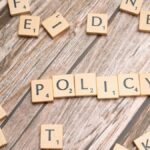 Scrabble letter tiles on a wooden background forming the word "Policy".