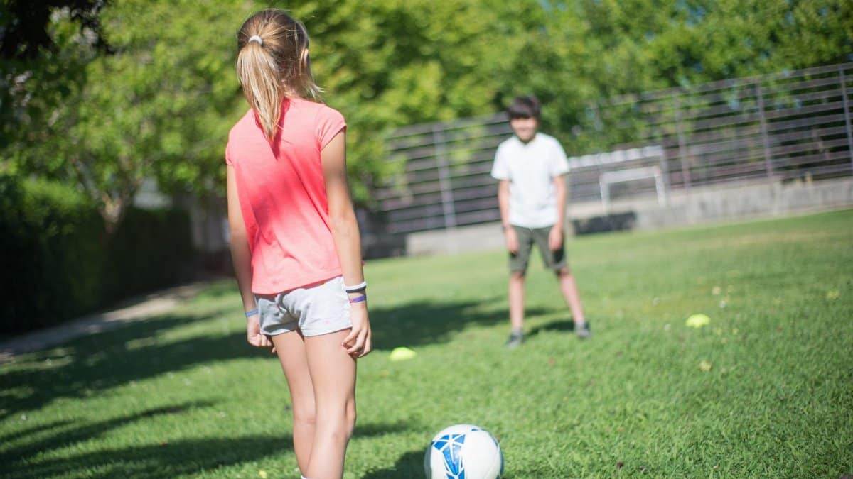 Kids having fun while playing soccer outdoors in a park on a sunny day.