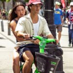 Couple enjoys a sunny ride on Lime scooter during a busy street scene in Seattle.