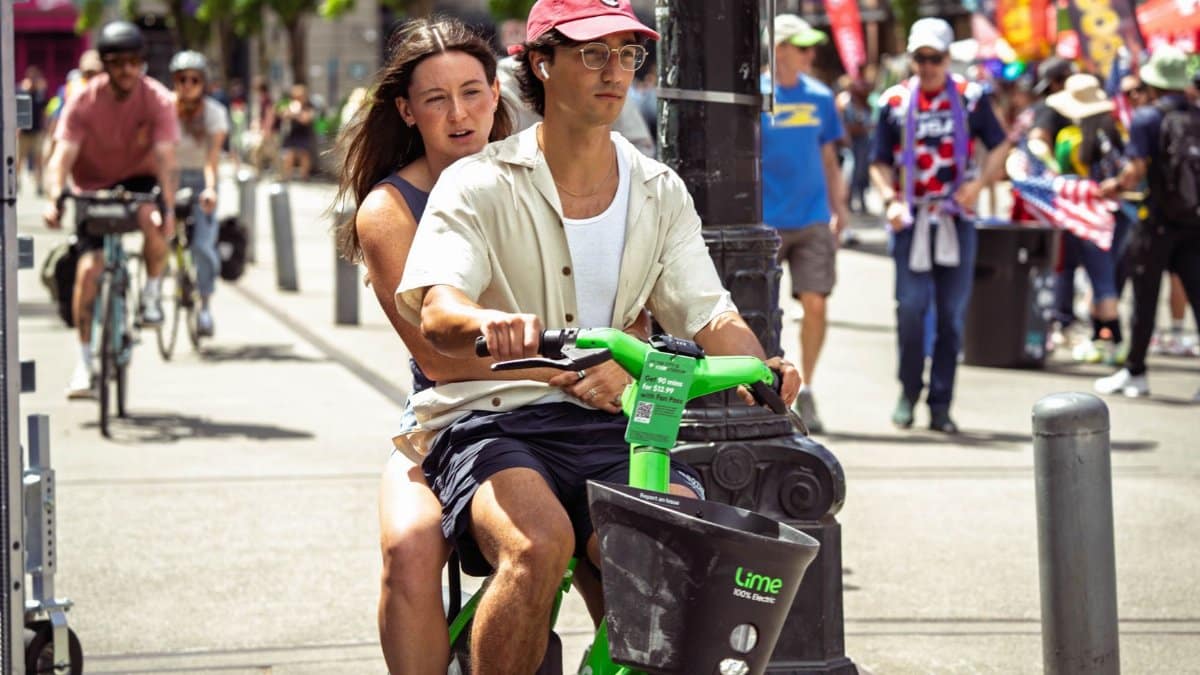 Couple enjoys a sunny ride on Lime scooter during a busy street scene in Seattle.