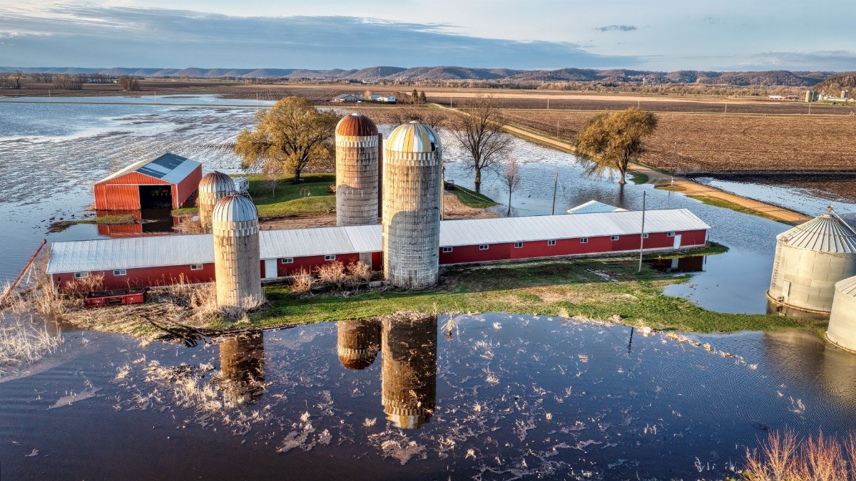 Aerial view of a flooded farm in Wabasha, MN, showcasing silos and barns in a rural landscape.