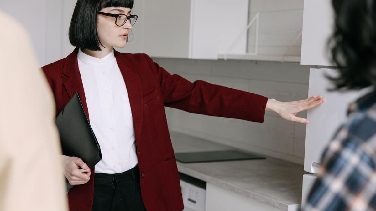 A female real estate agent demonstrates a modern kitchen to potential buyers in an apartment.