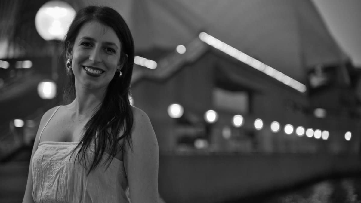 Smiling woman at Sydney Opera House, captured at night with a lively background.