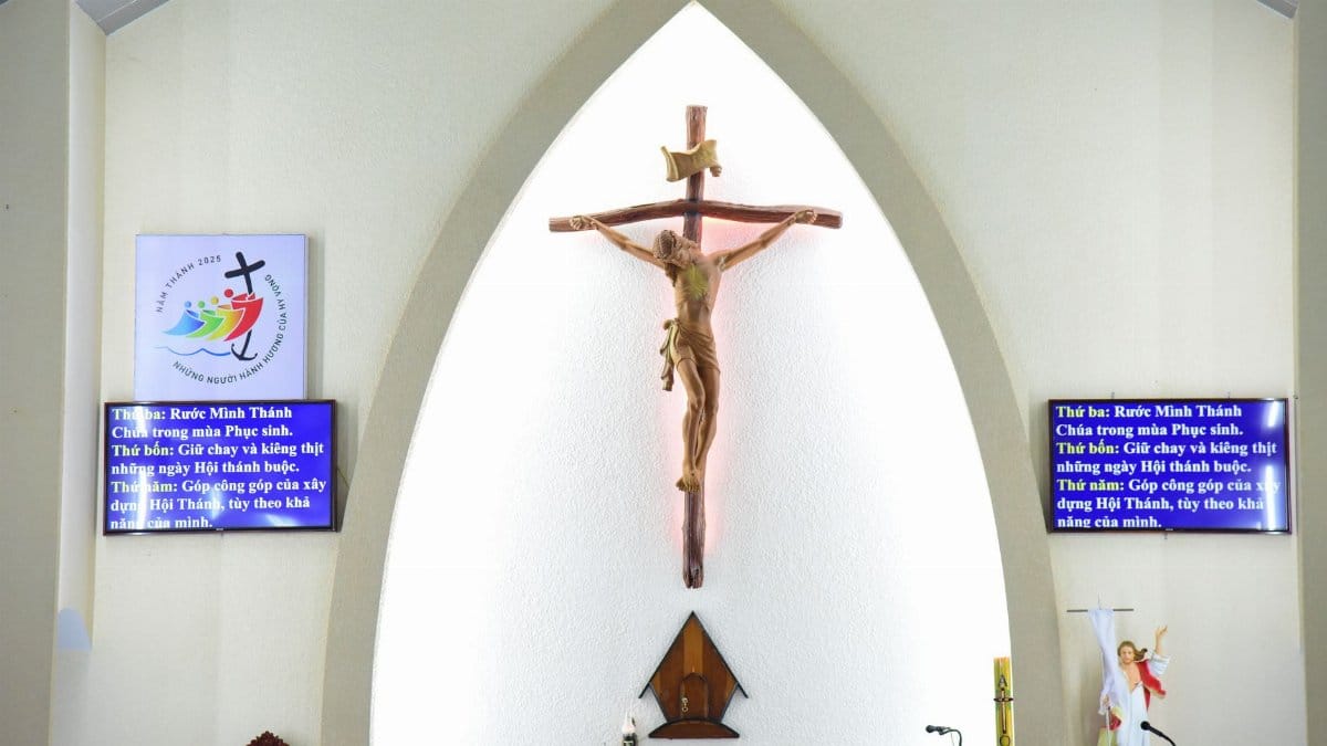 A serene church interior with a crucifix, flanked by digital screens displaying religious text.
