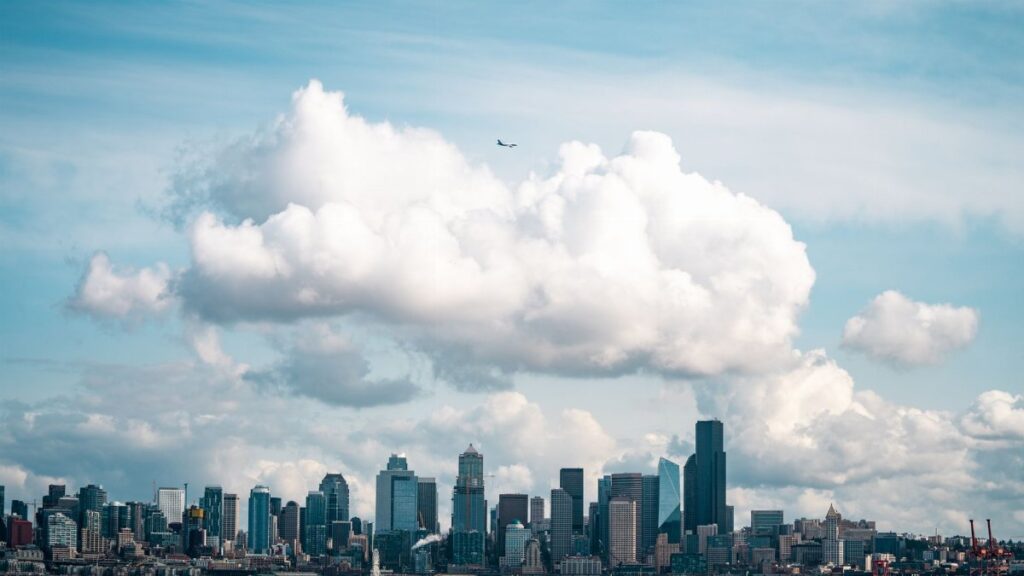 Dramatic aerial capture of Seattle's skyline with large clouds and a flying plane.