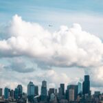 Dramatic aerial capture of Seattle's skyline with large clouds and a flying plane.
