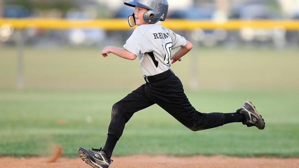 Action shot of a young baseball player running fast on the field, wearing uniform and helmet.