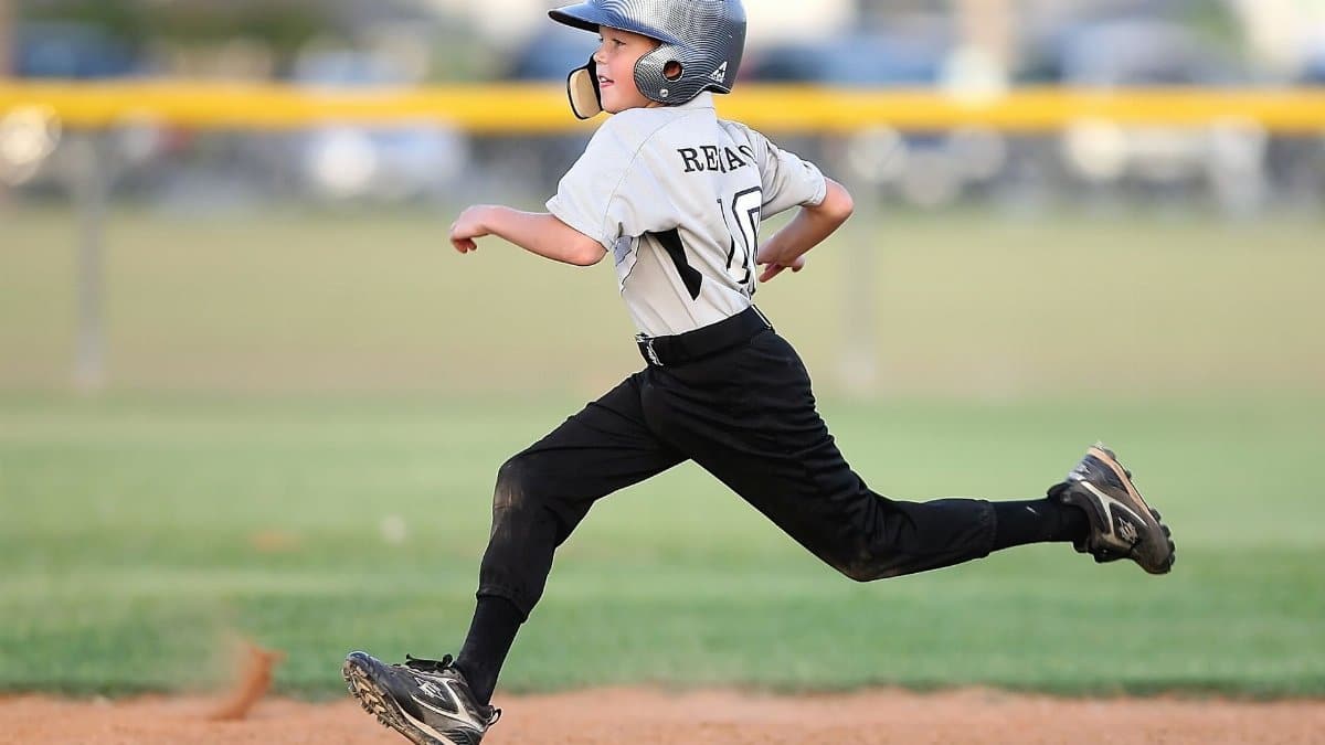 Action shot of a young baseball player running fast on the field, wearing uniform and helmet.