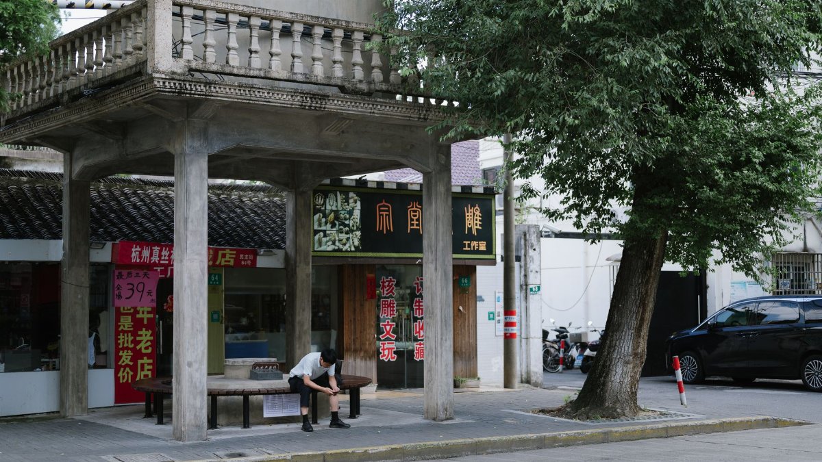 Street scene featuring a person sitting in front of local shops with cultural signage.