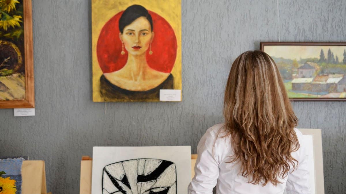 A woman views paintings in an art gallery, appreciating various art styles on display.