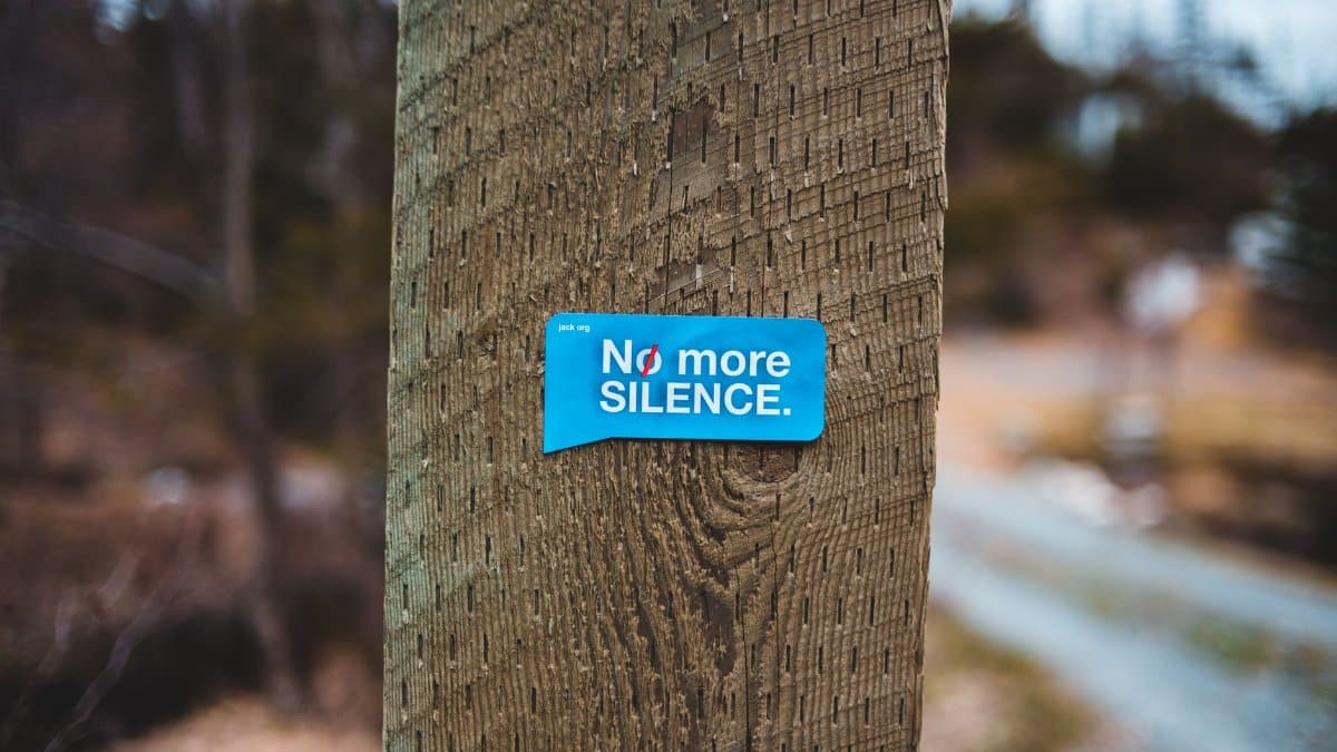 Social advertising inscription attached to trunk of tree growing near path under gray sky in gloomy weather