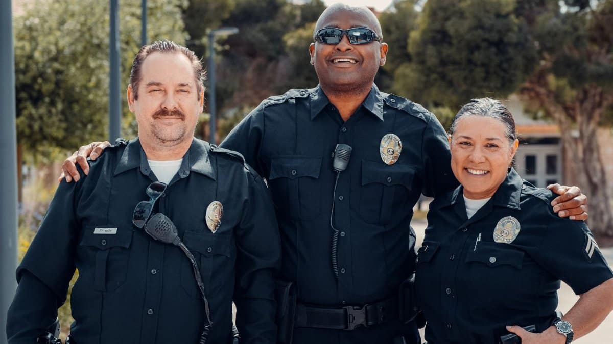 Three police officers in uniform smiling together outdoors, symbolizing community and law enforcement.