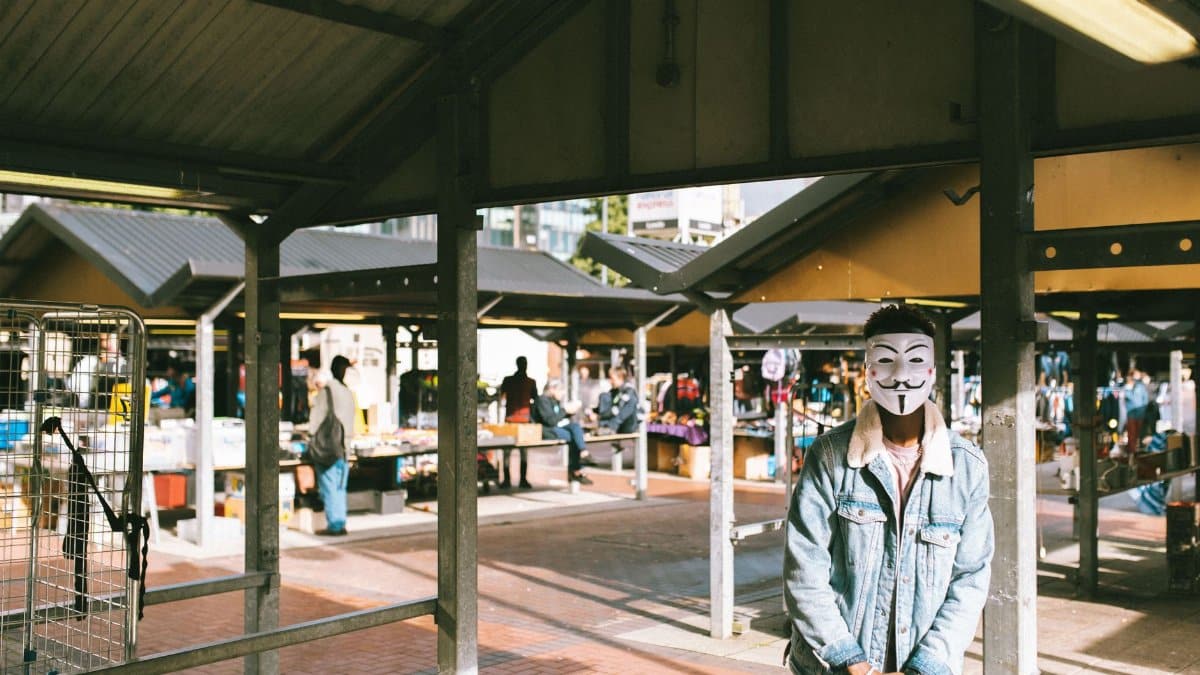 Unrecognizable black man in stylish clothes and Anonymous mask standing in local market in city and looking at camera in sunny day