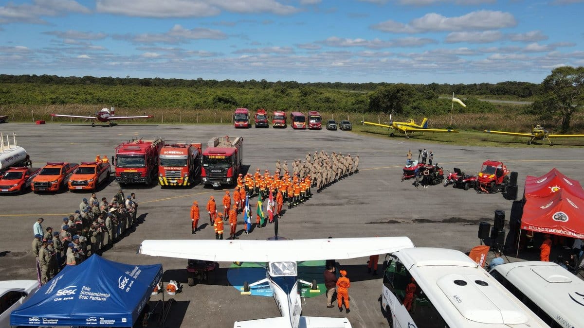 Aerial view of firefighters assembling with vehicles and aircraft at an airfield for wildfire management.