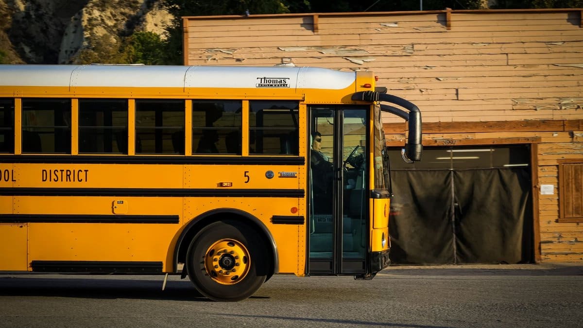 A classic yellow school bus parked on a city street with a rustic wooden building behind it.