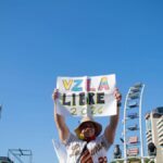 A person holds a sign reading 'VZLA Libre 2026' in a peaceful protest with a city backdrop.