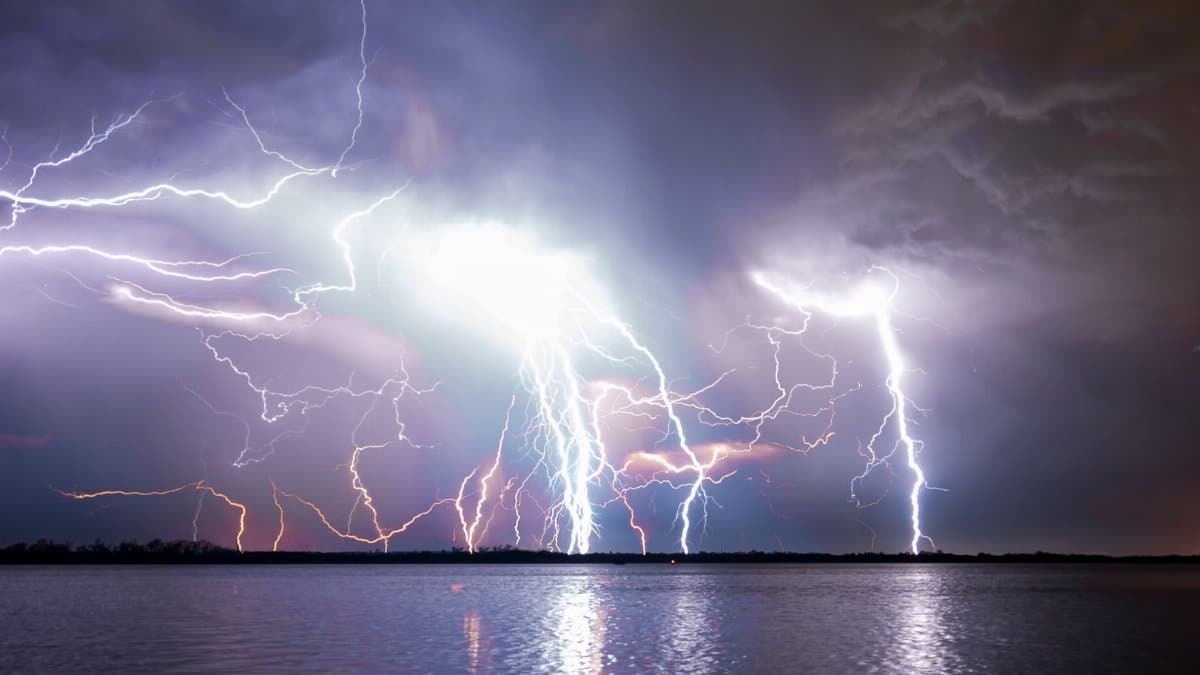 Dramatic long exposure of a lightning storm illuminating the night sky over a tranquil river.