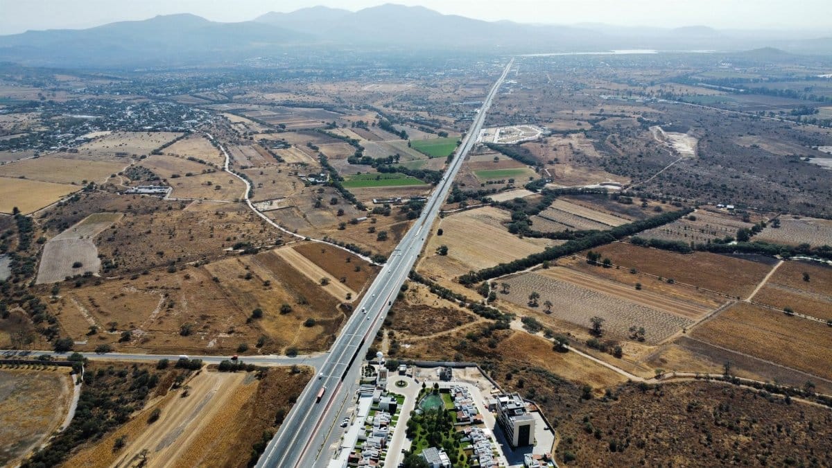 Drone shot of a long highway cutting through the picturesque Mexican countryside with surrounding fields.