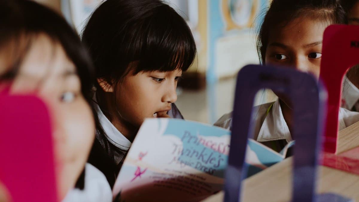 Group of children reading books together in a classroom setting.